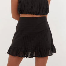 A black cotton skirt with a flared design and a thick elastic band at the base, featuring pin tuck details.