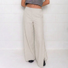 A person wearing high-waisted, wide-leg pants with thin vertical pinstripes in a light beige/cream color, paired with a gray plaid crop top and black shoes, standing against a white tiled wall.