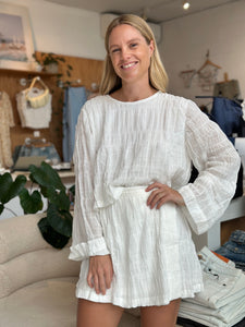 long sleeve top and short white skirt on girl standing in store with hand on hip