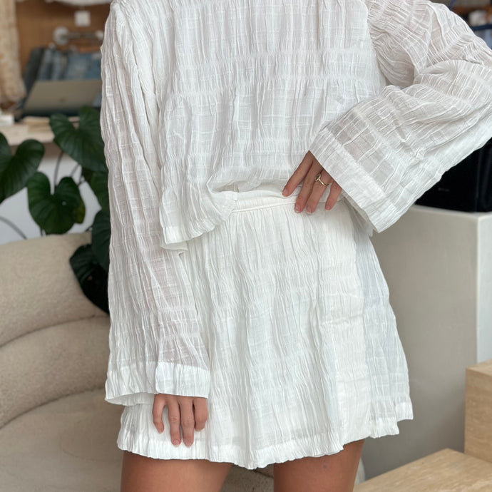 long sleeve top and short white skirt on girl standing in store with hand on hip