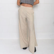A pair of beige Bermuda pants with a high waist and mid-thigh slit, worn by a model against a white brick wall.