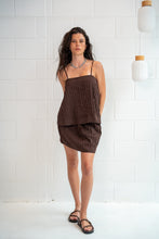 Woman wearing a brown dress standing against a white tiled wall.
