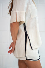 Person wearing a white outfit with black trim against a white tiled wall.