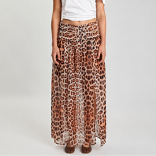 A model stands against a light gray studio background wearing a white one-shoulder cropped top and a long leopard-print skirt in brown, beige, and black.