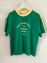 Green t-shirt with yellow accents and text on a white brick wall background